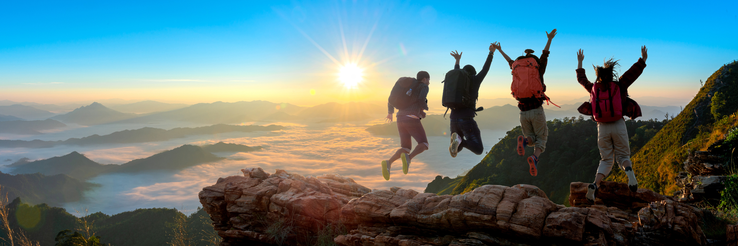 Groepje dat in de lucht springt met uizticht op bergen en zonsondergang
