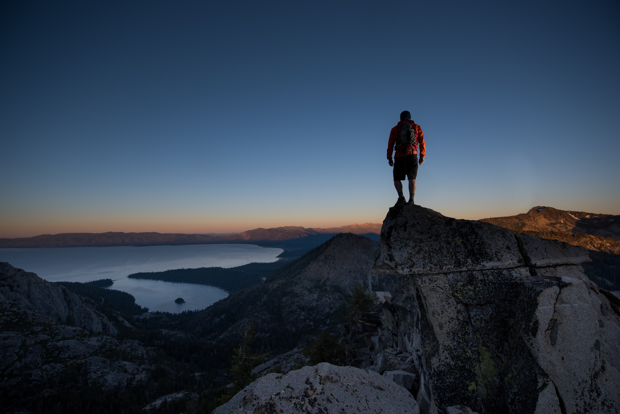 Persoon die bovenop bergtop staat en uitkijkt op water en zonsondergang