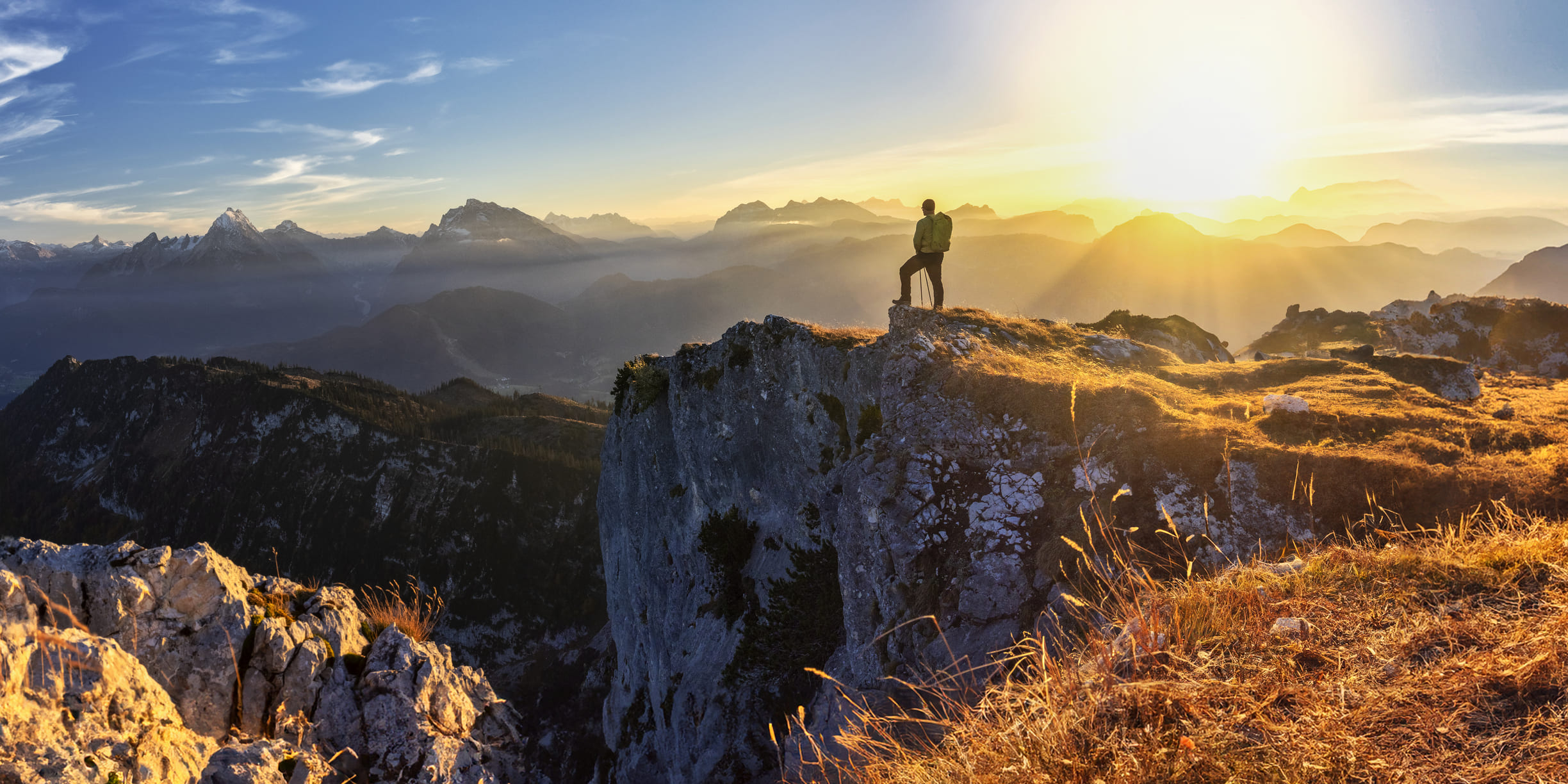 Persoon die trots op een berg staat met de zon en zonsondergang op de achtergrond
