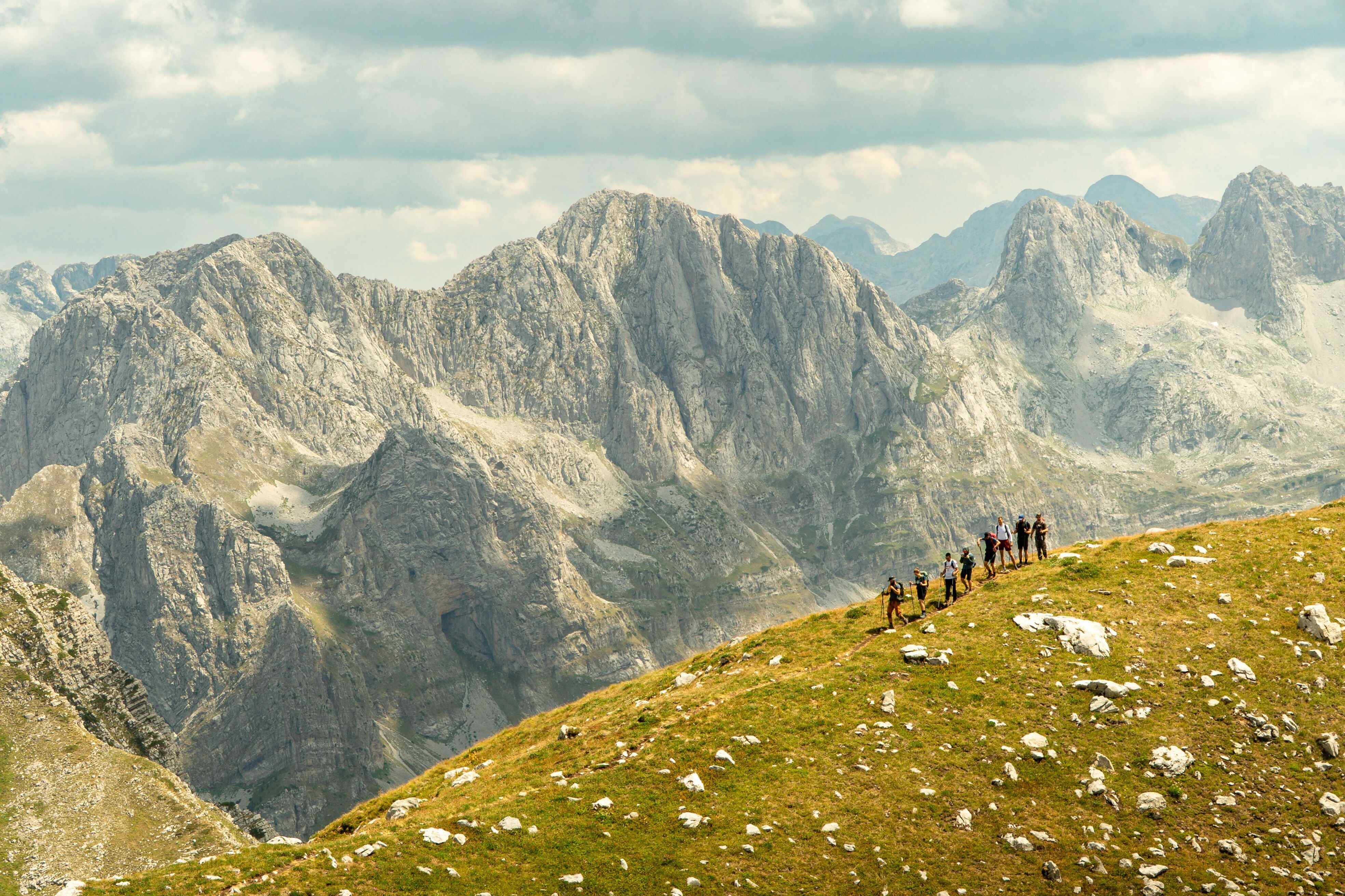 Groep wandelaars die een berg afwandelen met een hele bergketen in de achtergrond